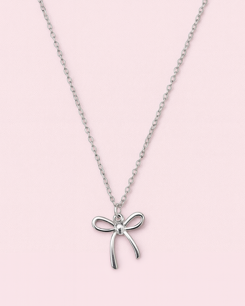 Silver necklace with a bow pendant on a pink background