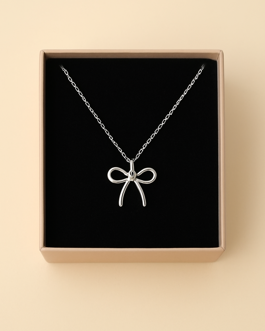 Silver necklace with a bow pendant in a box on a beige background