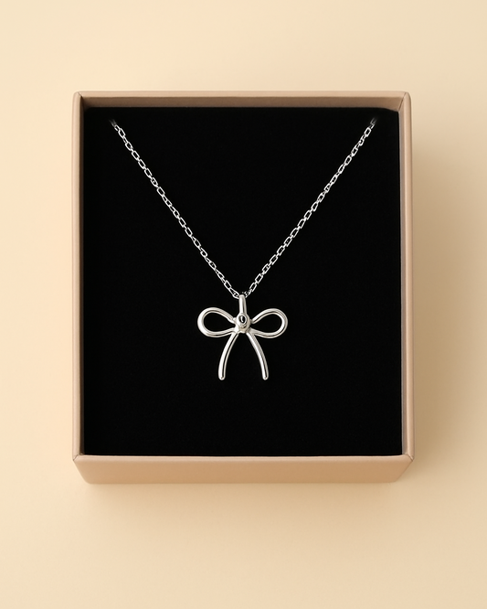 Silver necklace with a bow pendant in a box on a beige background
