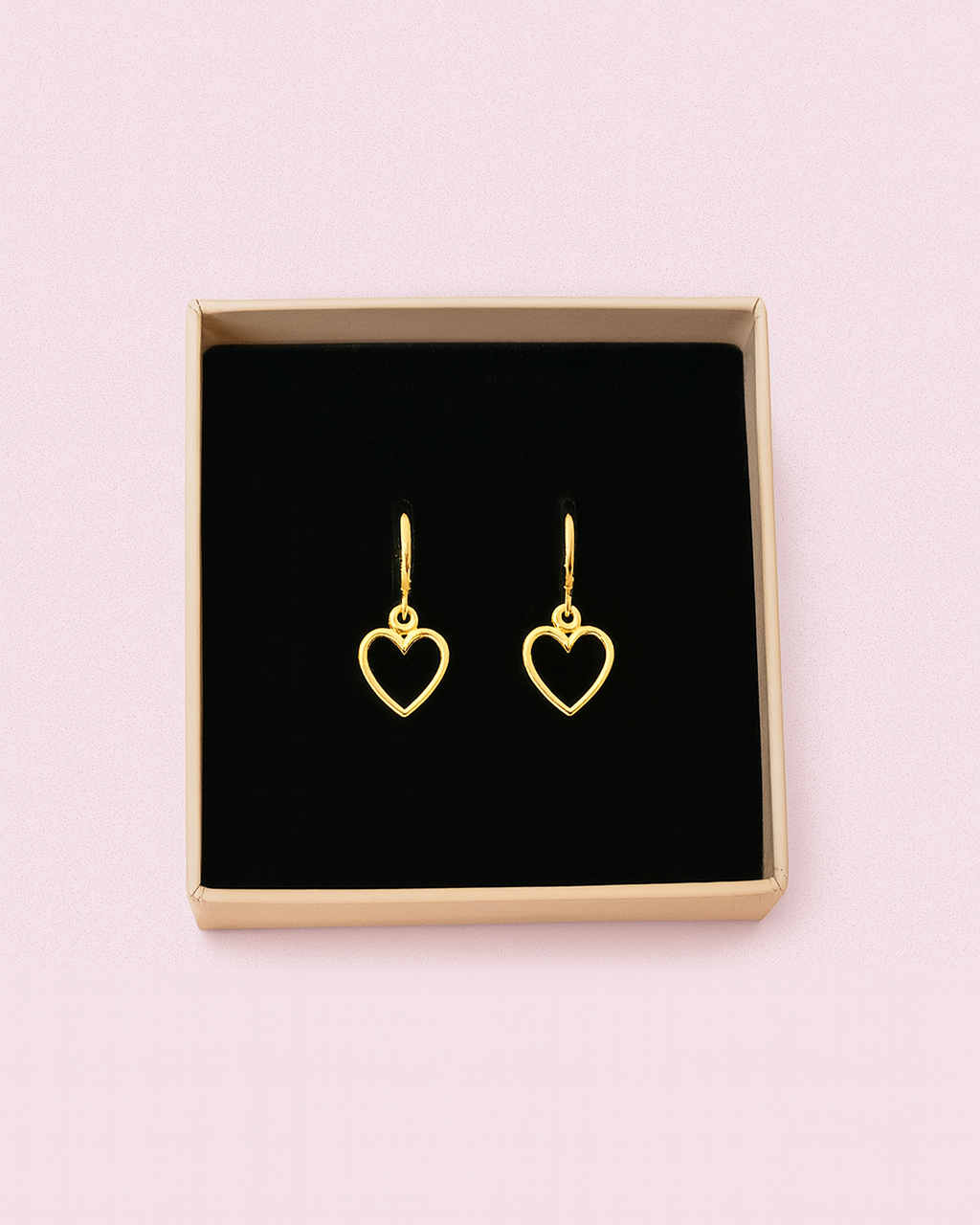 Heart-shaped gold earrings in a black box on a pink background