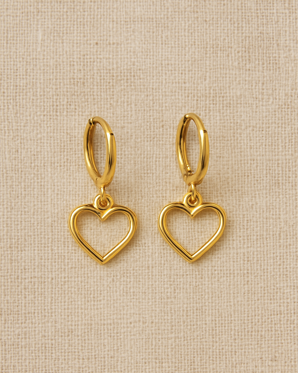 Gold heart-shaped earrings on a beige fabric background