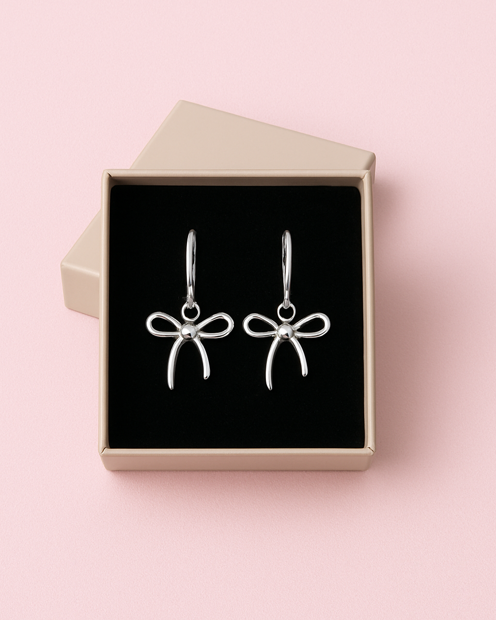 Silver bow-shaped earrings in a jewelry box on a pink background