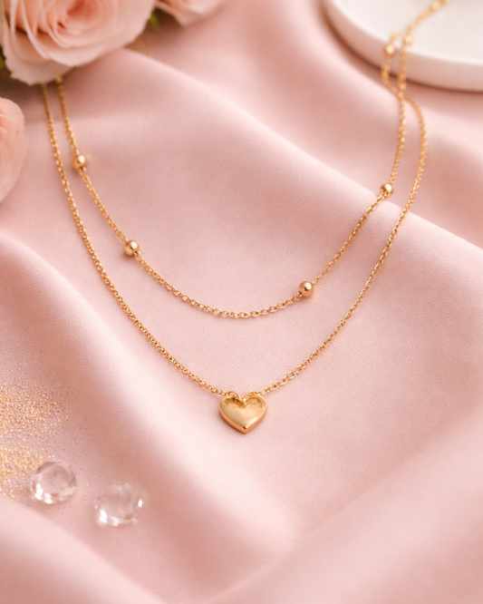 Gold necklace with a heart pendant on a pink fabric background